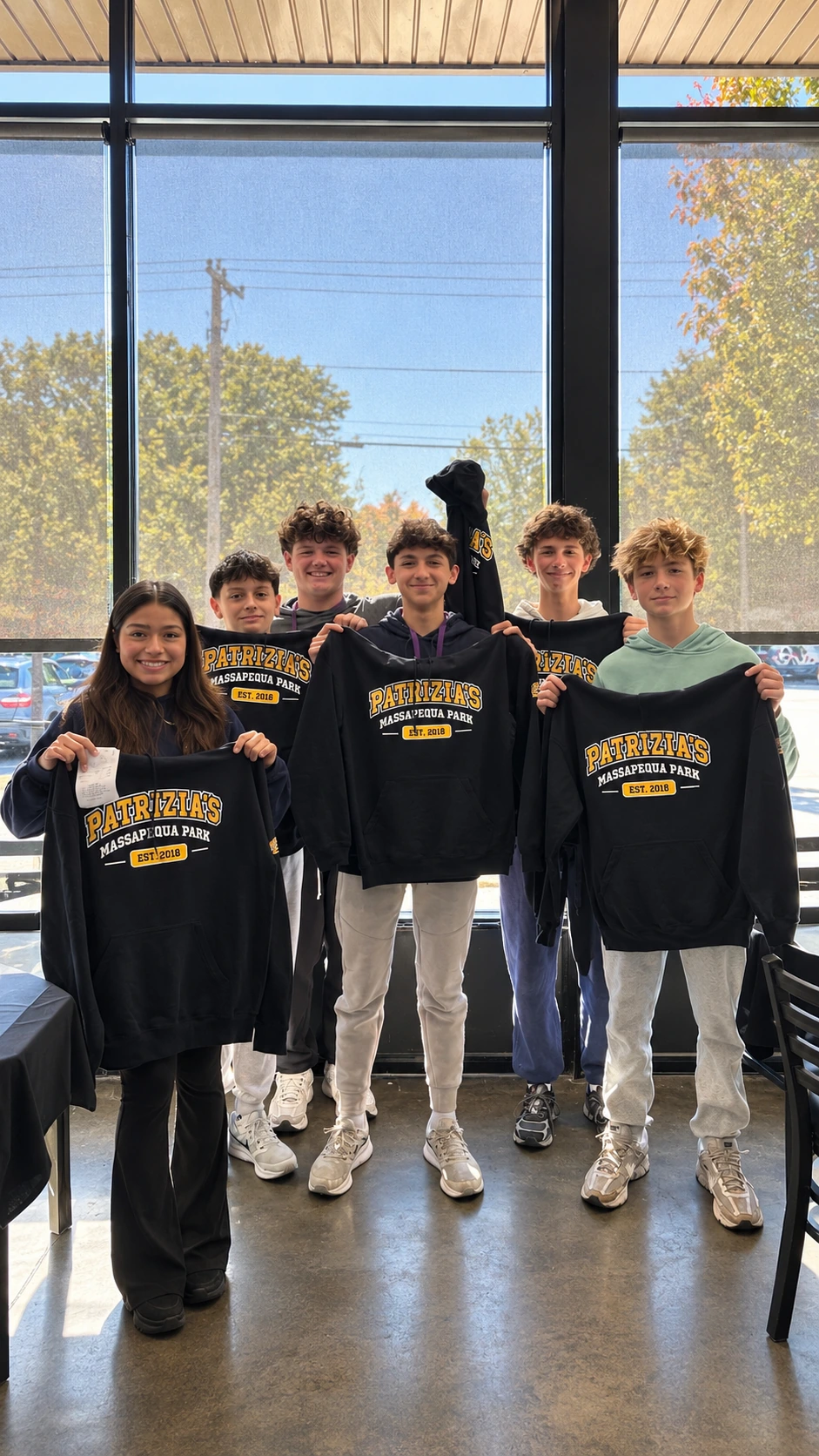 Six smiling students holding their earned Patrizia’s hoodies inside the restaurant